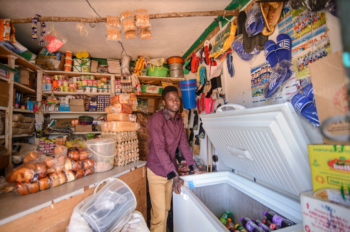 A man stands behind a refrigeration unit in a corner shop 