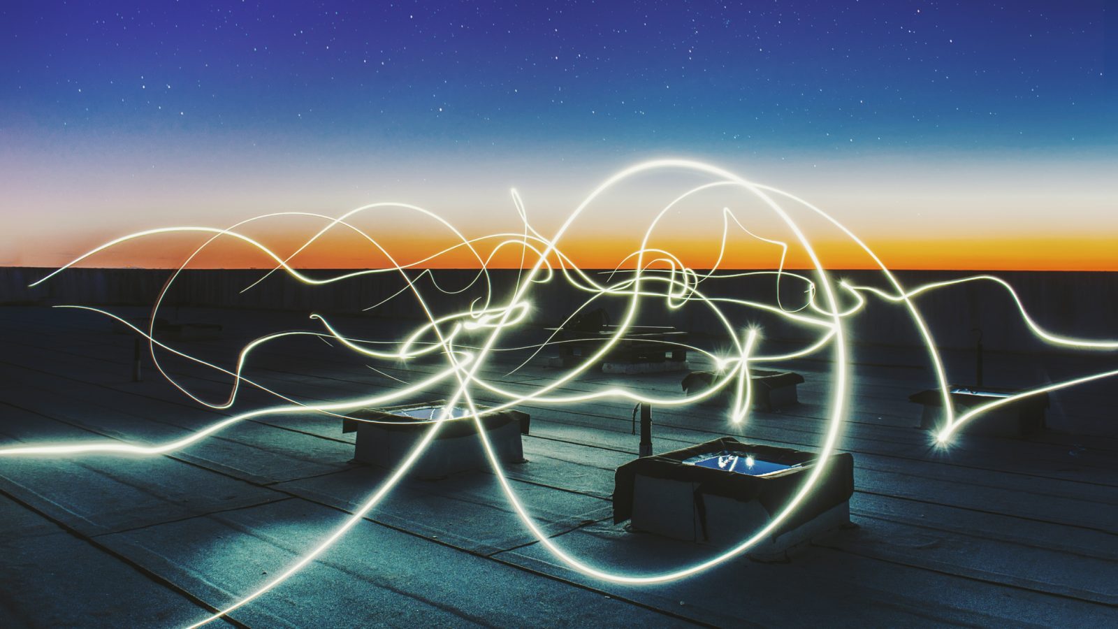 Twirling lines of electric light streak across a rooftop
