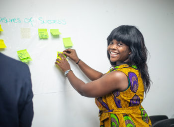 A woman smiles as she puts post-it notes onto a whiteboard