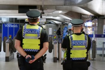 Two men in police uniform stand with their backs facing the camera in a tube station