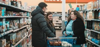 Two women and a man stand around a trolley in the middle of a supermarket