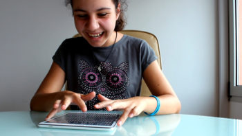 A young girl in a grey t shirt with an owl picture on it uses a tablet
