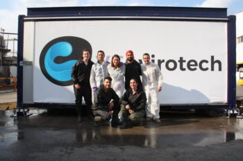 A group of people stand outside in front of a large sign saying VEnvirotech