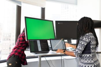 Two women working on computers with multiple monitors