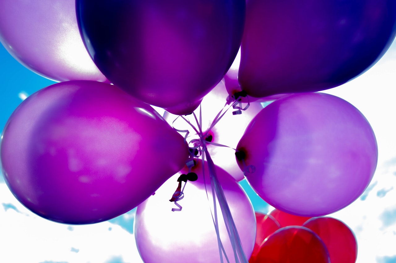 A bunch of purple and balloons float against a cloudy blue sky