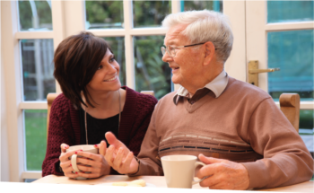 A younger woman on the left and an older man on the right have tea and enjoy a chat.