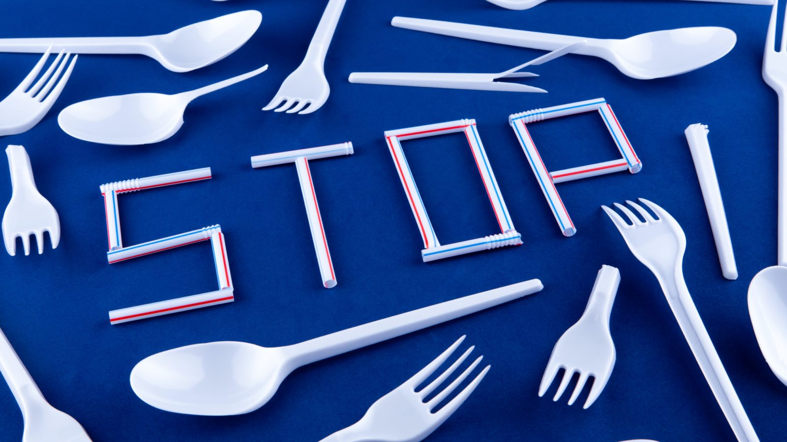 A table is scattered with plastic cutlery and plastic straws spell out the word 'STOP'