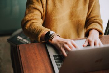 A close up of a woman in a yellow jumper working at a laptop