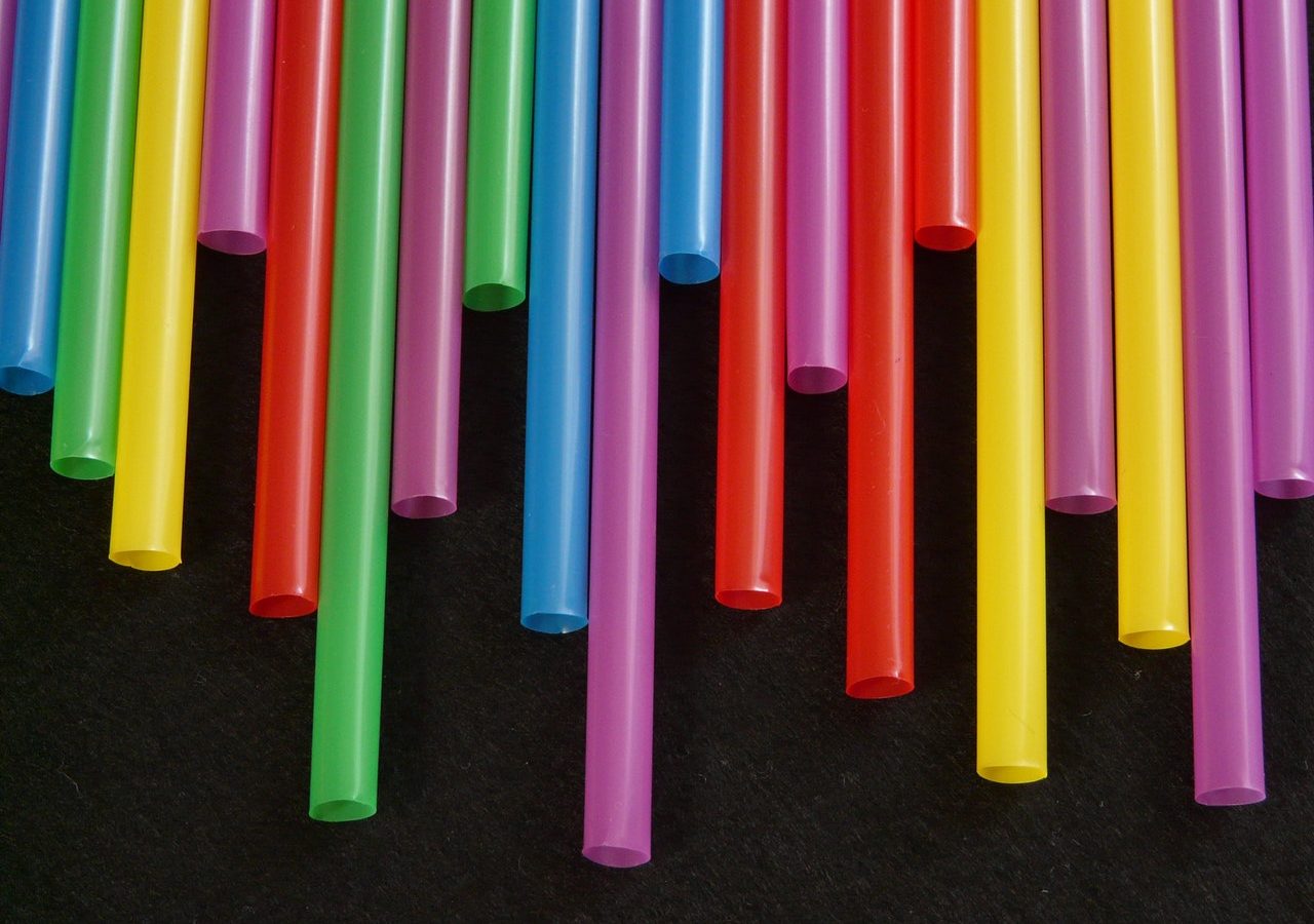 Coloured straws of different lengths are lined up to form an uneven curtain against a black background