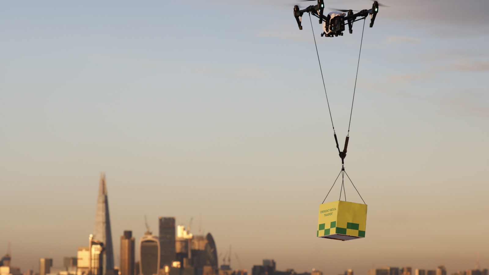 A quadcopter drone flies over London carrying a box of supplies or aid