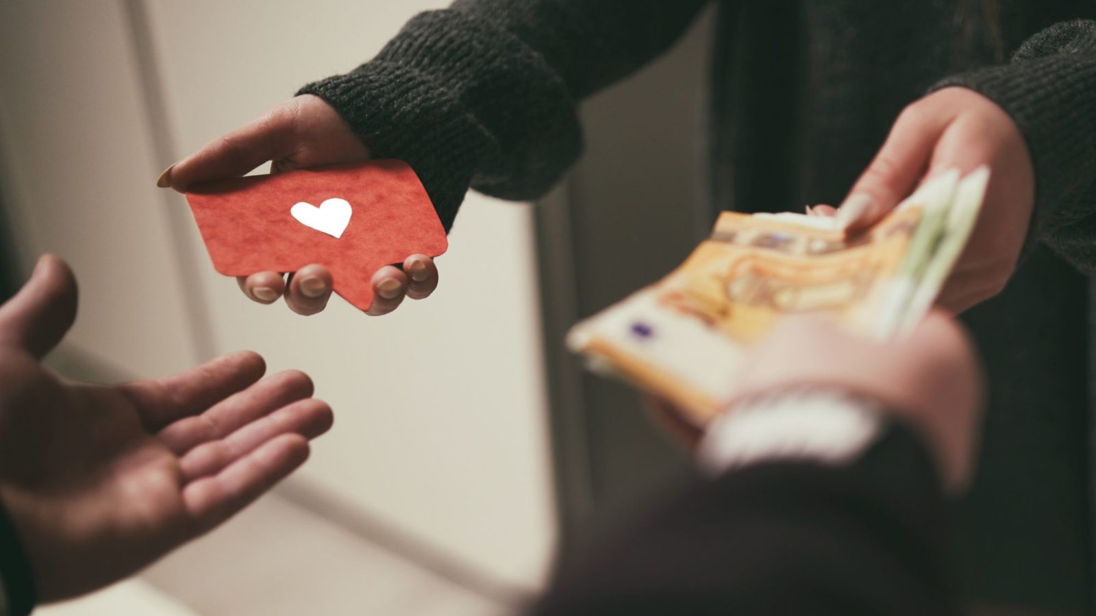 Close up of two pairs of hands mid-transaction. Exchanging money for a card with a heart image on it.