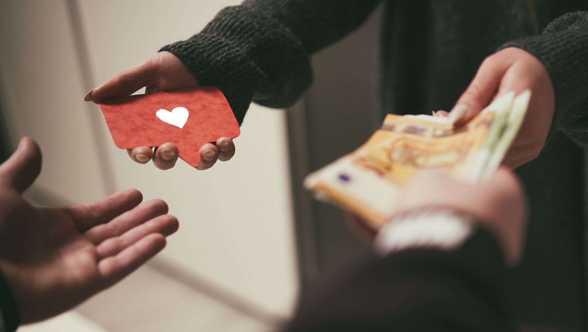 Close up of two pairs of hands mid-transaction. Exchanging money for a card with a heart image on it.