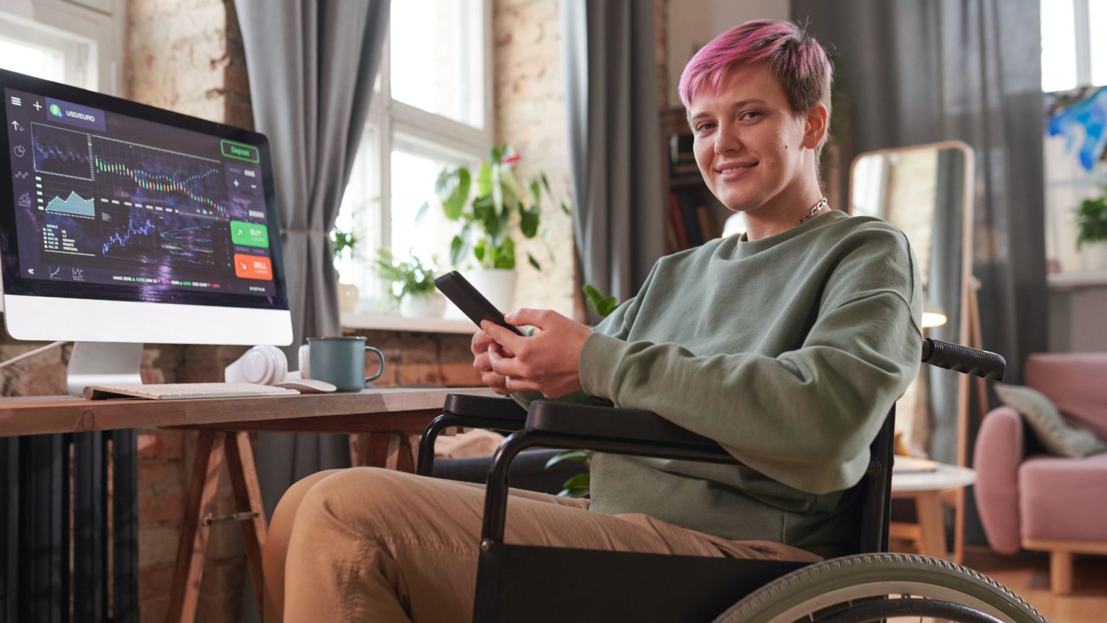 A bright airy warehouse style apartment, charts displayed on screen, person sat in wheelchair typing into phone