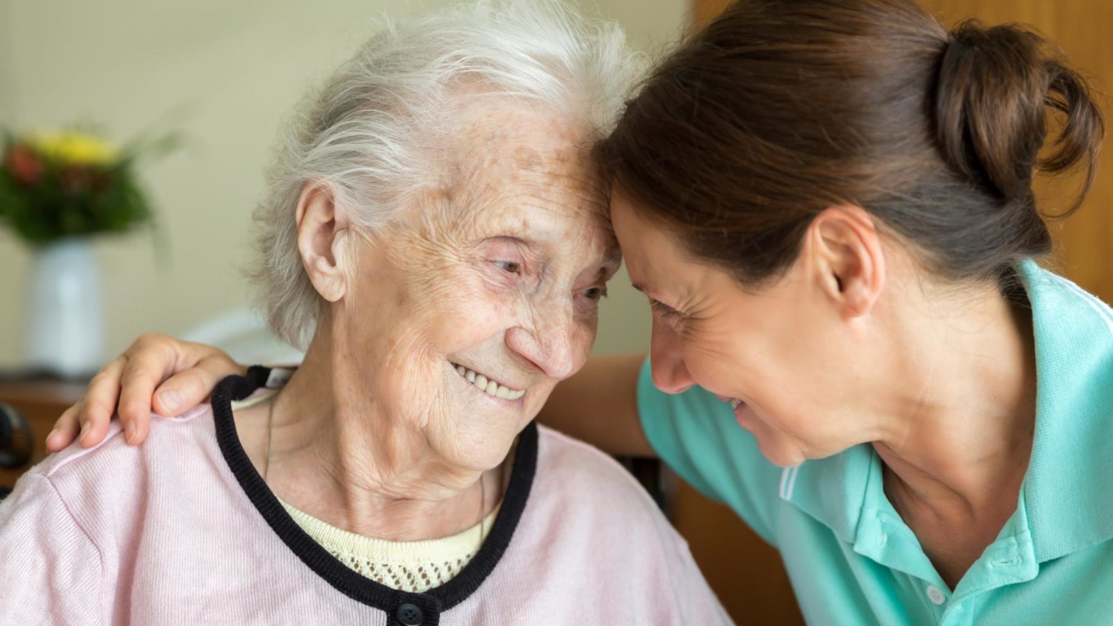 Older lady smiling with carer in scrubs