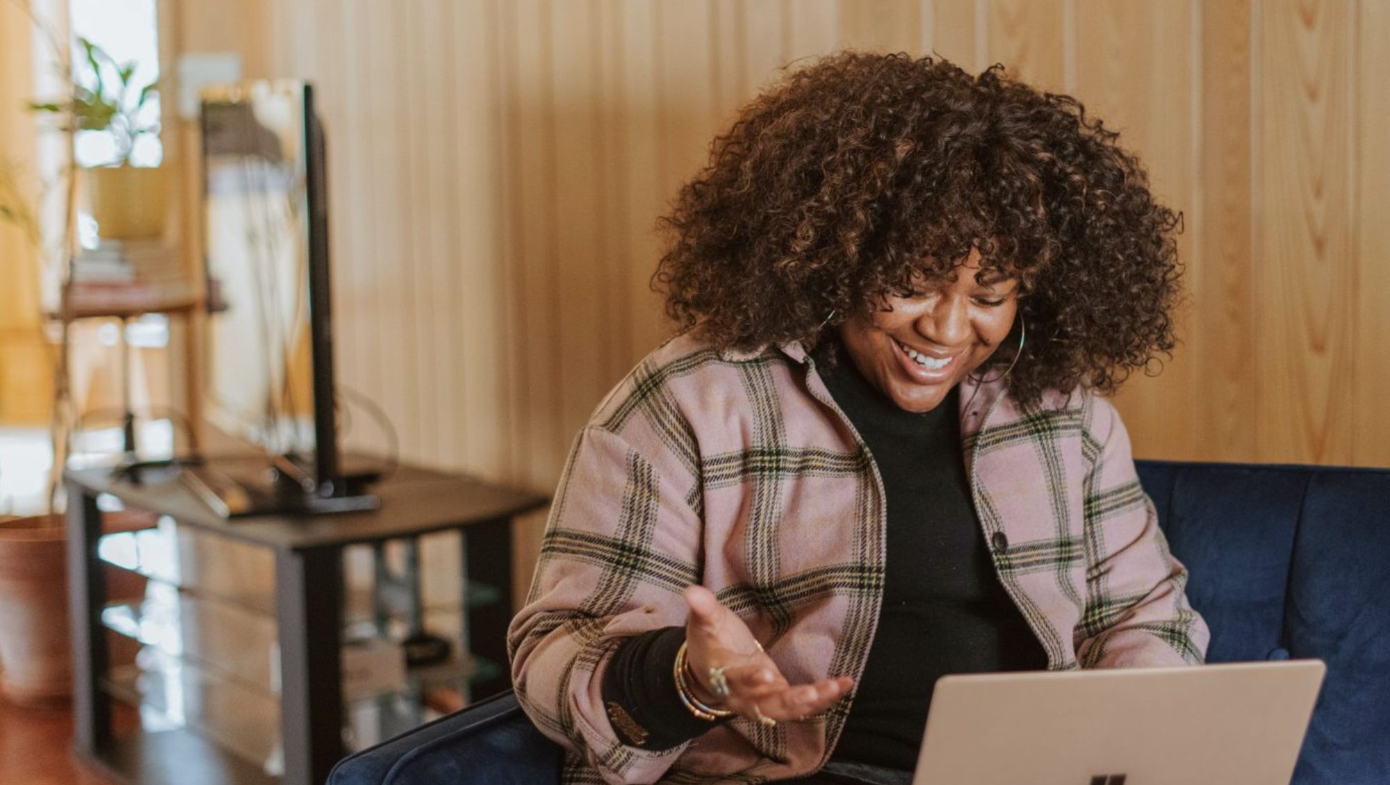 Sat at home on a sofa smiling at the laptop on their lap