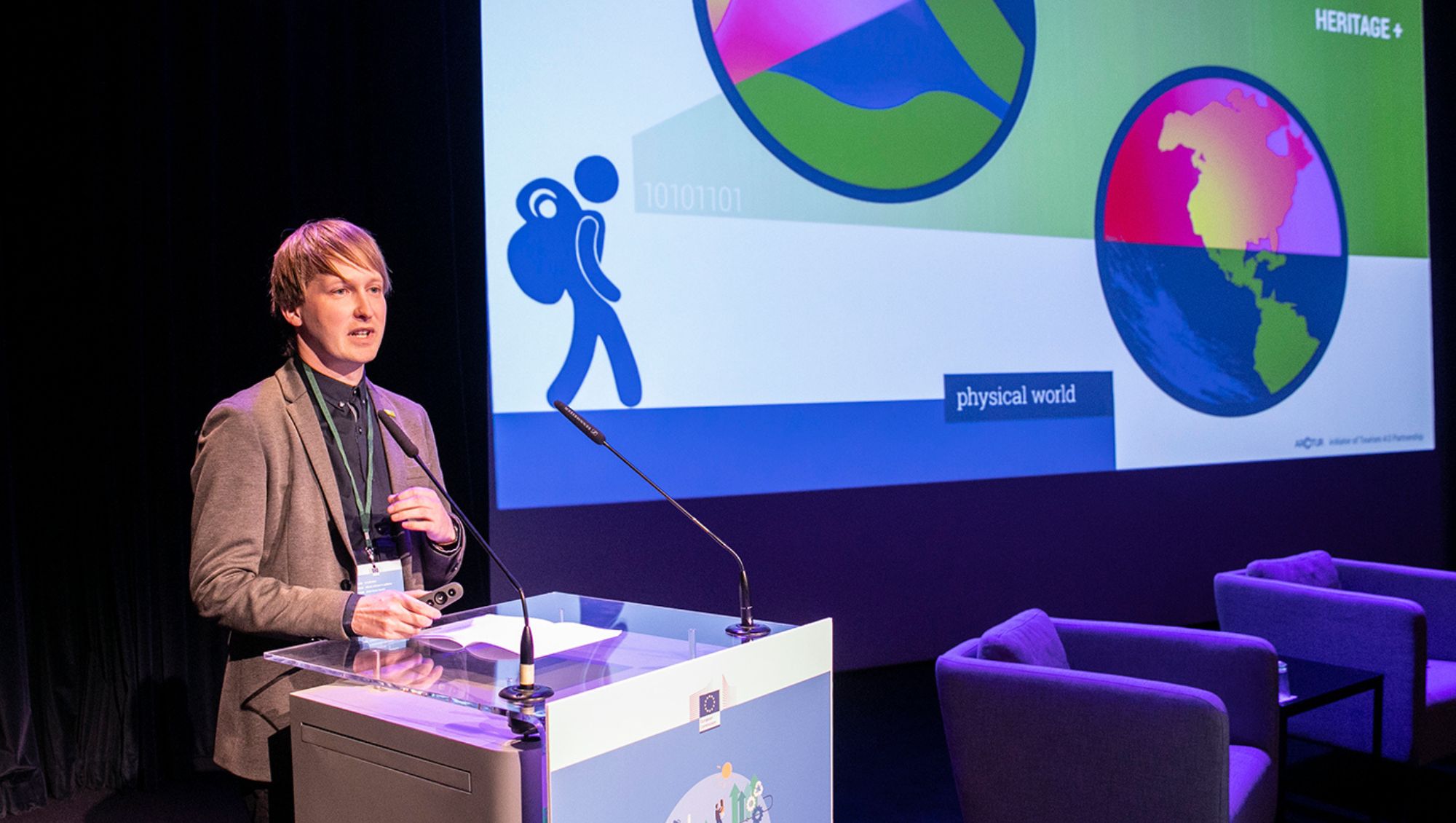 Speaker at a conference stands at podium, projected on large screen is illustration of a man with a bag looking at the world from different perspectives