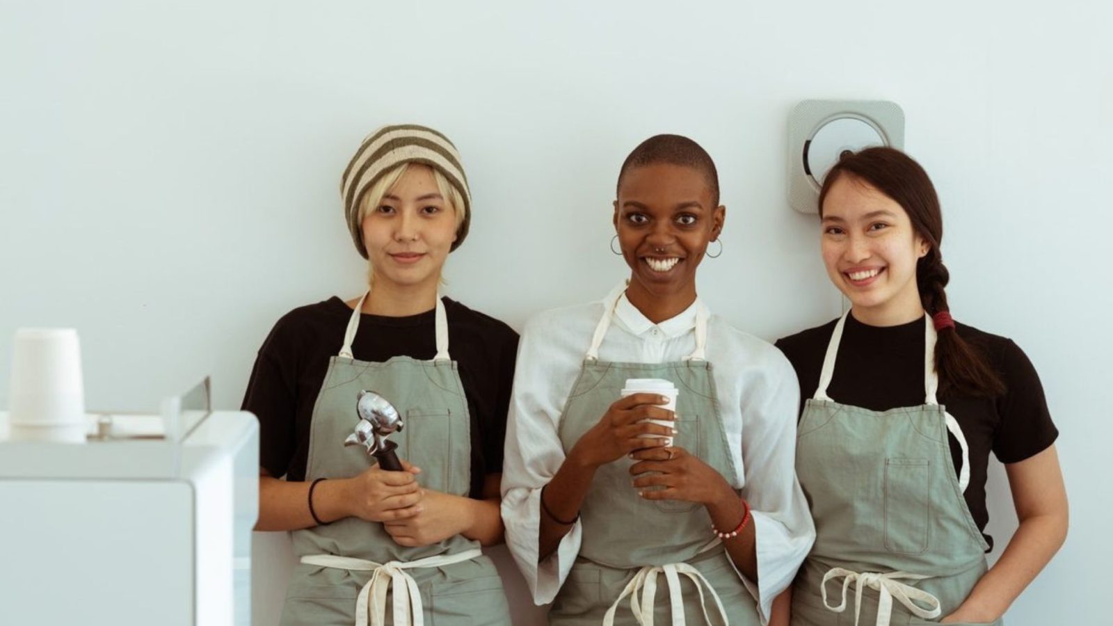 Three smiling baristas in matching light khaki aprons