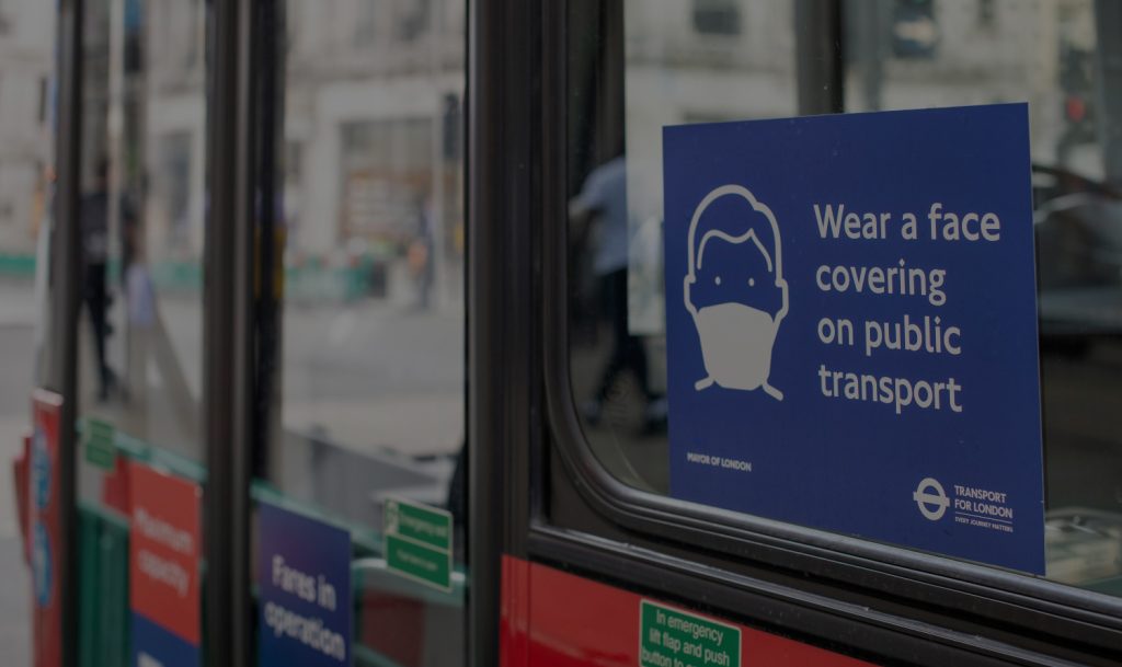 A close-up shot of the side of a London bus, with a sign instructing people to wear masks on public transport