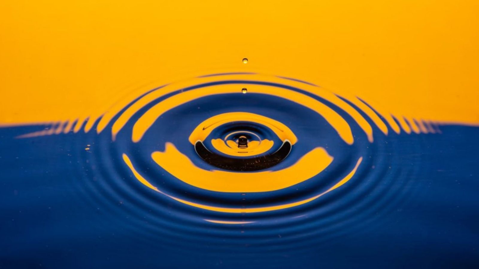 Water reflecting orange and blue ripples as water droplets hit the surface and bounce