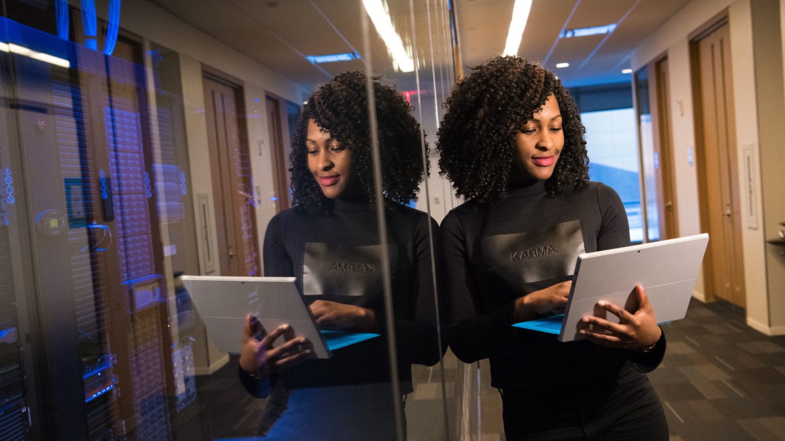 Woman rests against a reflective office window typing on her laptop