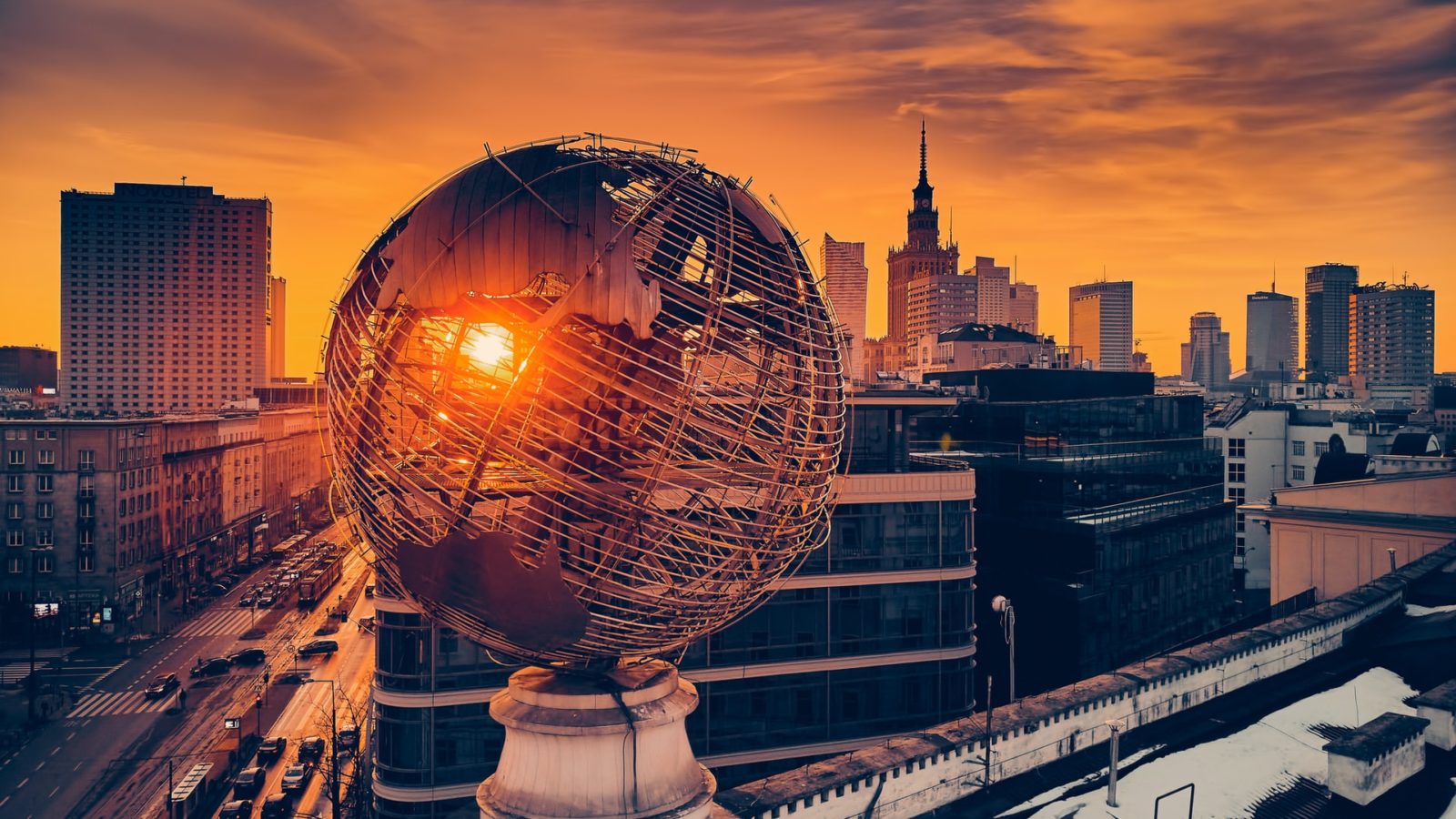 Globe statue against a city backdrop, with the sun setting on the horizon