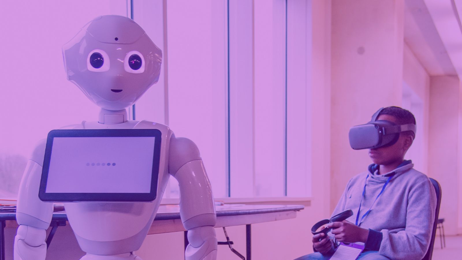 Boy sitting down with a VR headset on which is connected to and controlling a white humanoid robot