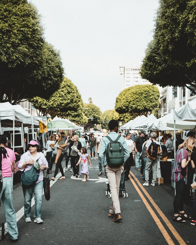 People walking through an outdoor market, lined with trees