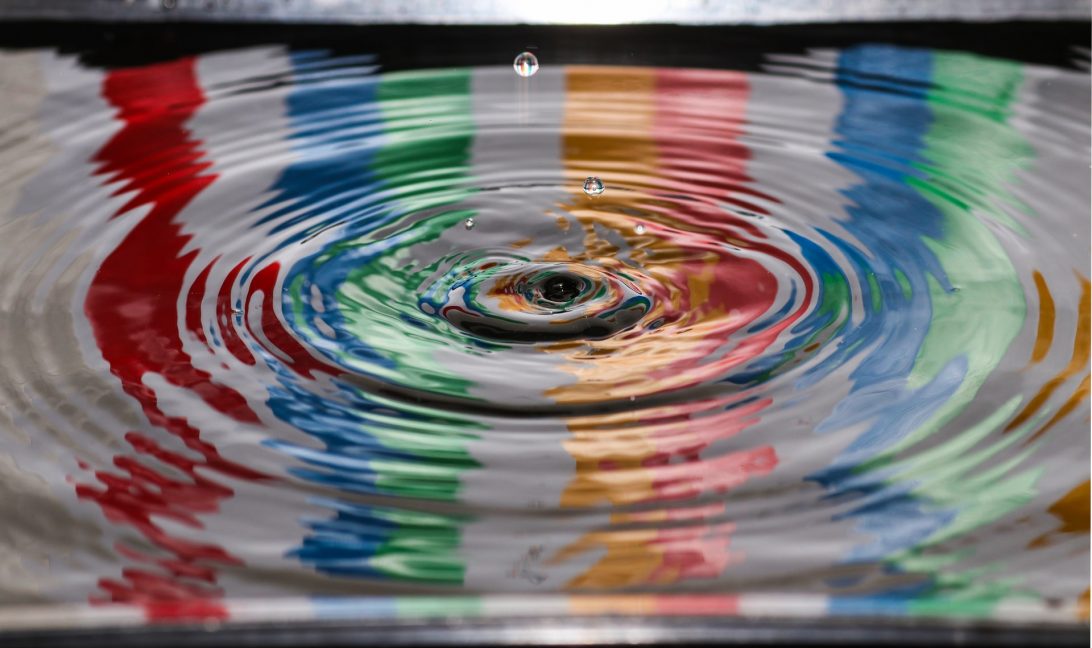 A droplet of water entering a pool that is reflecting rainbow colours