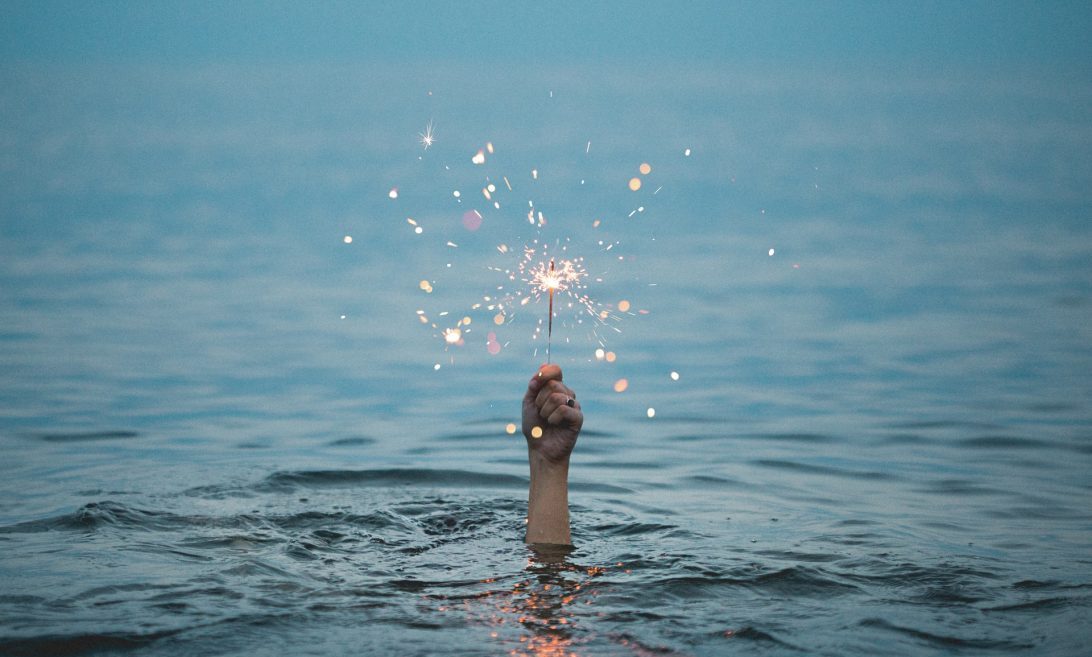 A hand emerges from a lake and holds a sparkler
