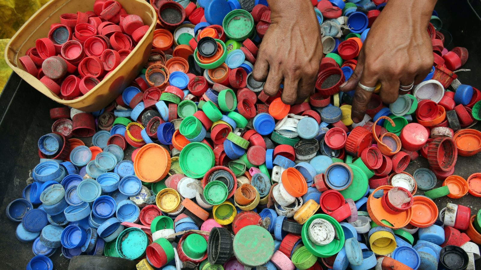 A pair of hands sorts through a collection of bottle caps