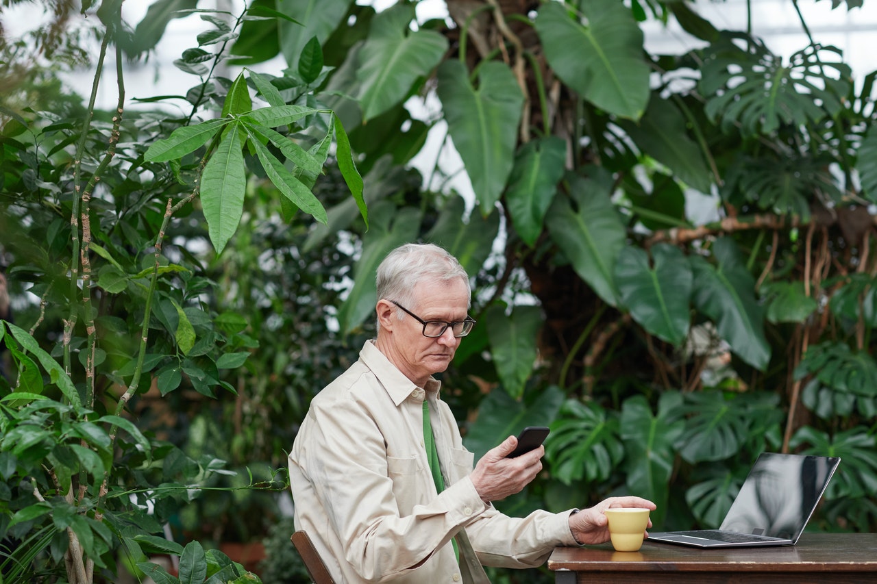 Older man looking at his smartphone against a backdrop of lush foliage
