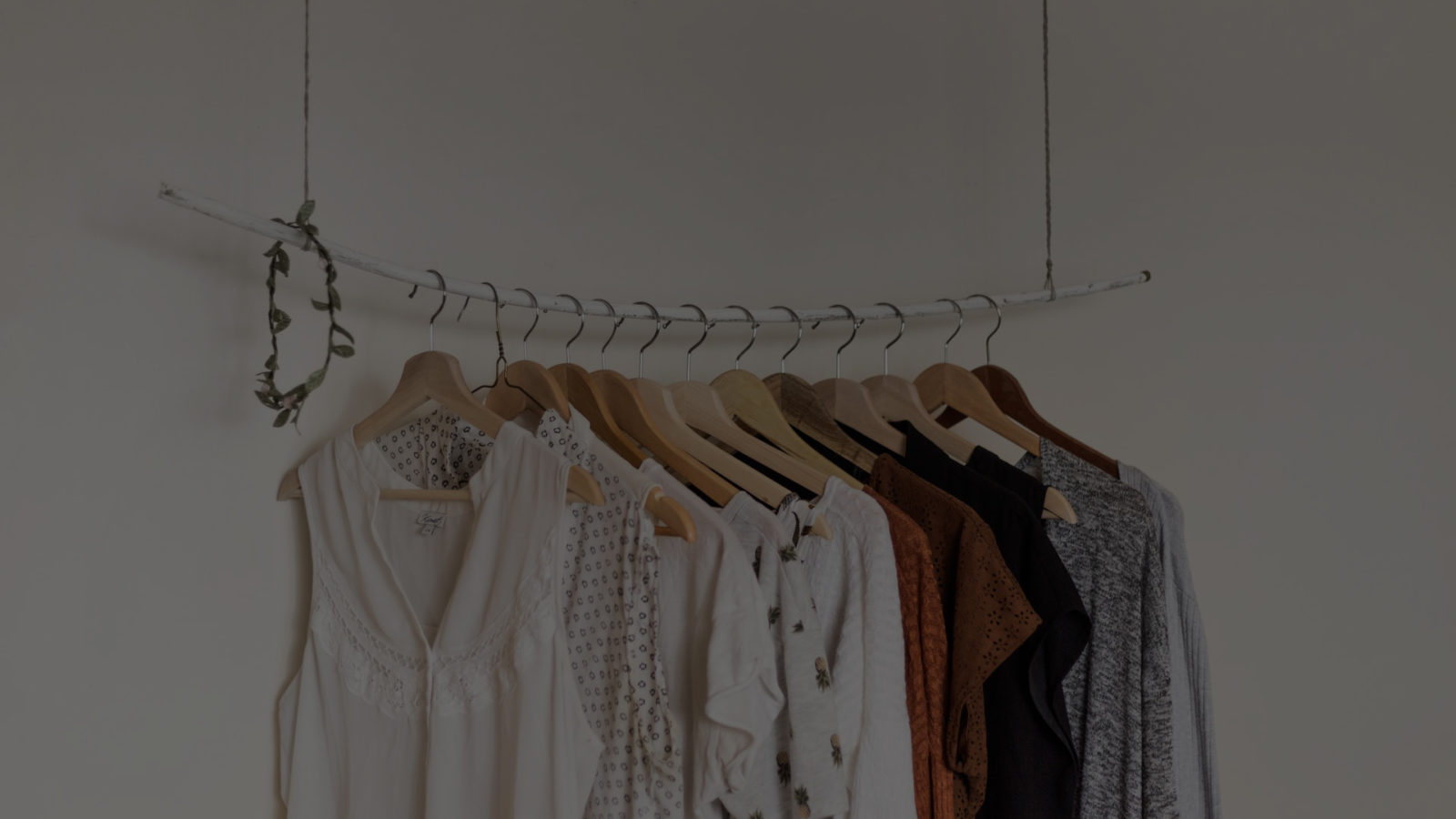 A silver rail of neutral coloured clothes, hung on wooden hangers