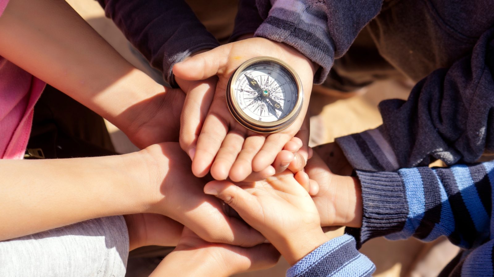 Hands of young children palms upright cradling a compass in the sunshine