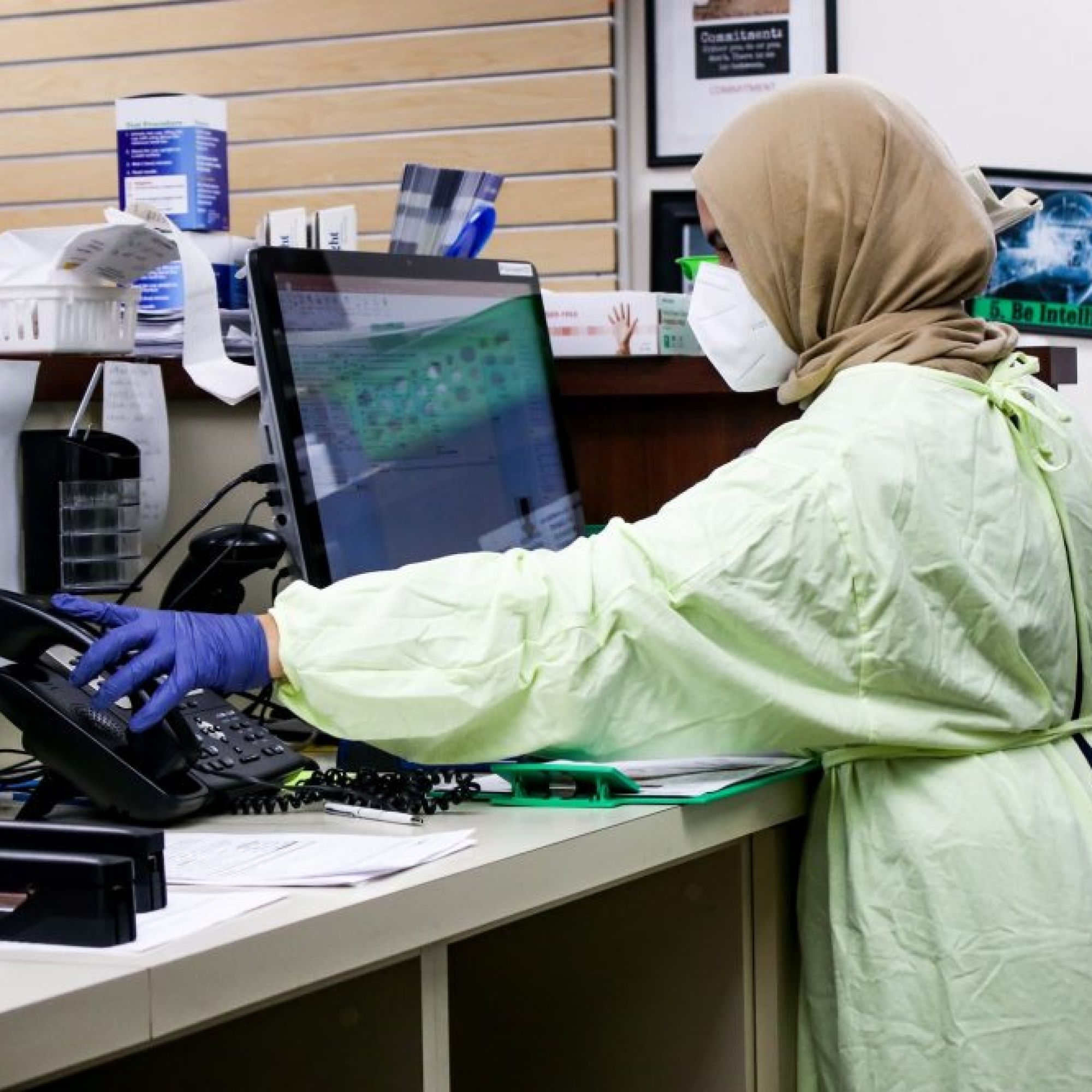 Lady wearing full PPE and hijab answers phone with hand in a bright blue glove
