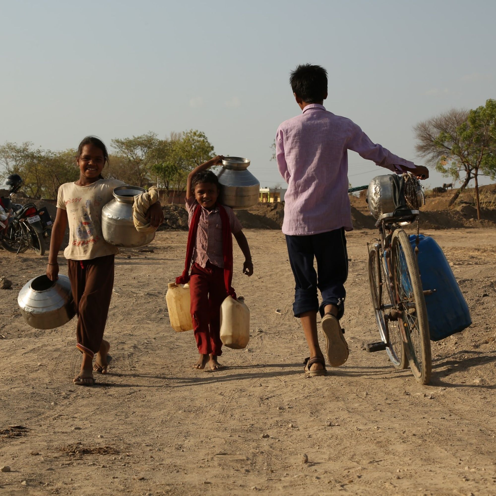 Children carrying water by hand and on bicycle along a dry and dusty road