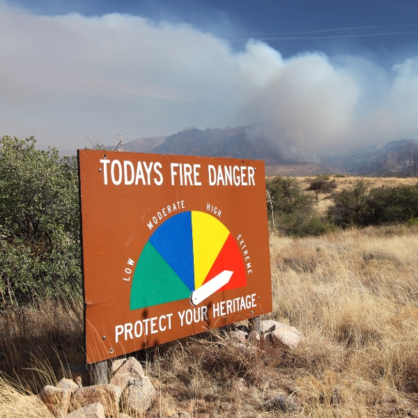 On dusty grass near dry shrug with smoke billlowing behind a anger of wildfires sign points to the most serious level warning in Organ Mountains New Mexico