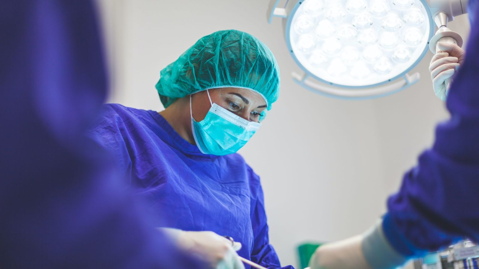 A surgeon in blue and purple scrubs performs surgery