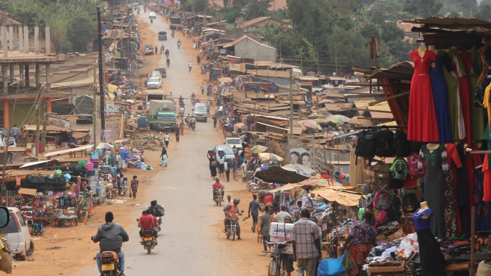 A busy dirt road with motor bikes and people on the side selling items of clothing