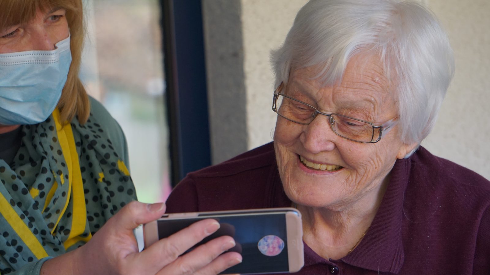 A grey haired woman looks at a phone