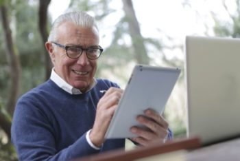 An older man uses an ipad and smiles to camera