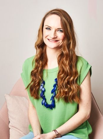 Photograph of a white woman with long red hair and a green top