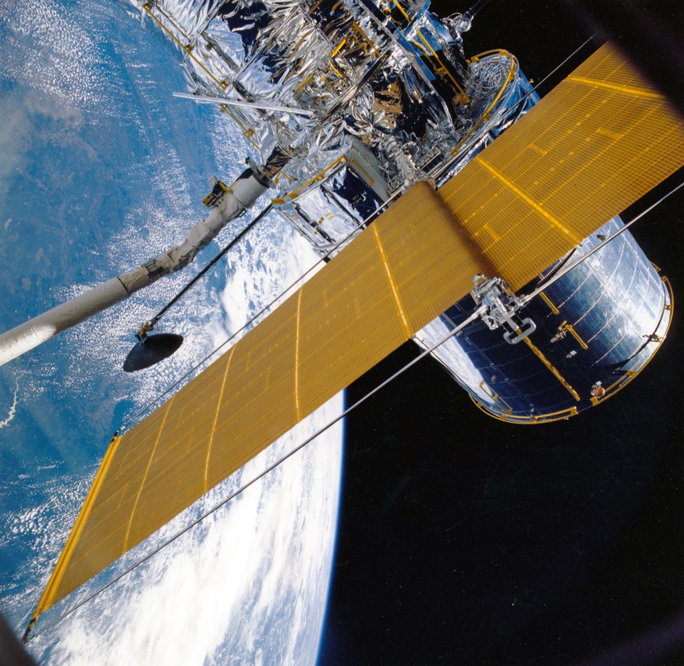 A satellite with a yellow sail flies above the earth through space