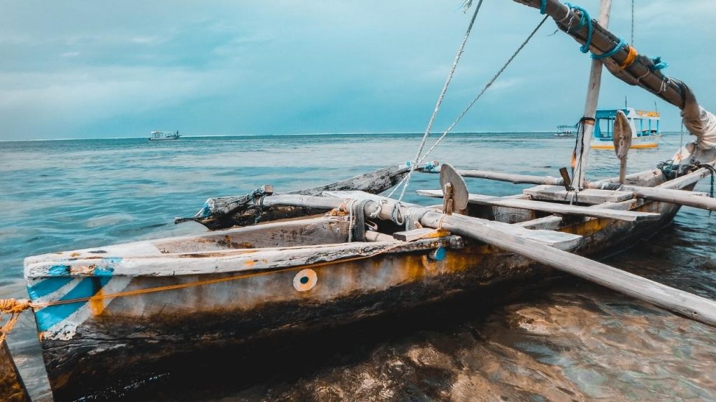 A long boat sails down resting on the shore-as blue sea stretches into the horizon.