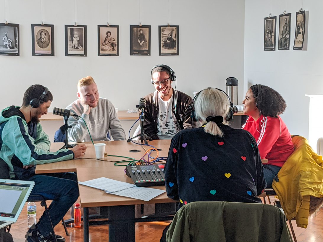 People sitting around a table recording a podcast|Thrive LDN logo - towards happier