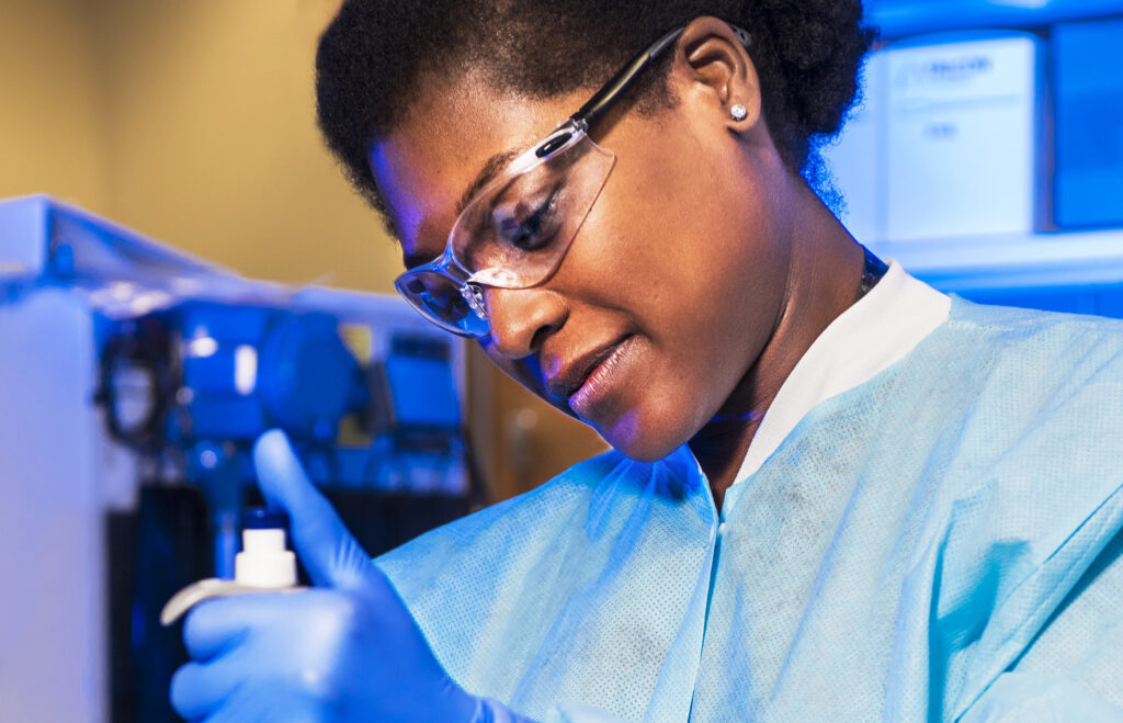 person with dark skin in glasses and scrubs pipetting into vials|person with dark skin in glasses and scrubs pipetting into vials
