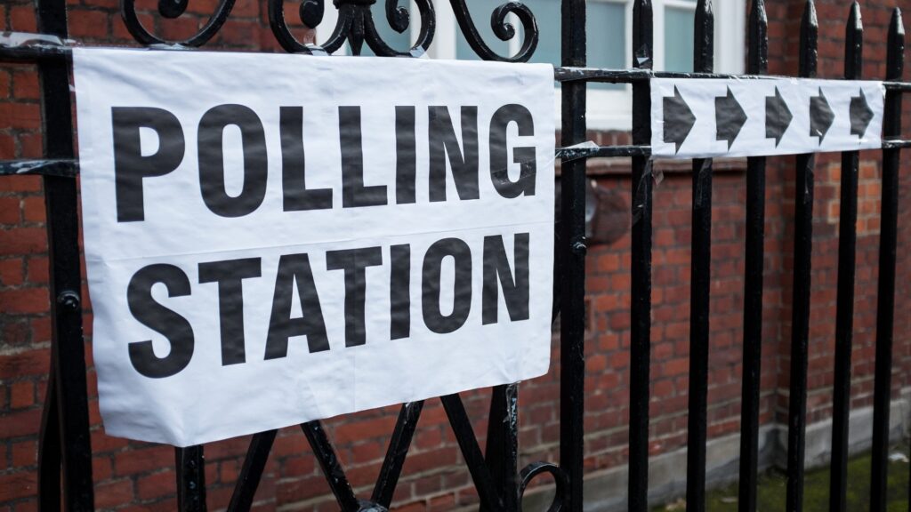 Democracy in the UK - polling station sign and arrows displayed on a metal fence