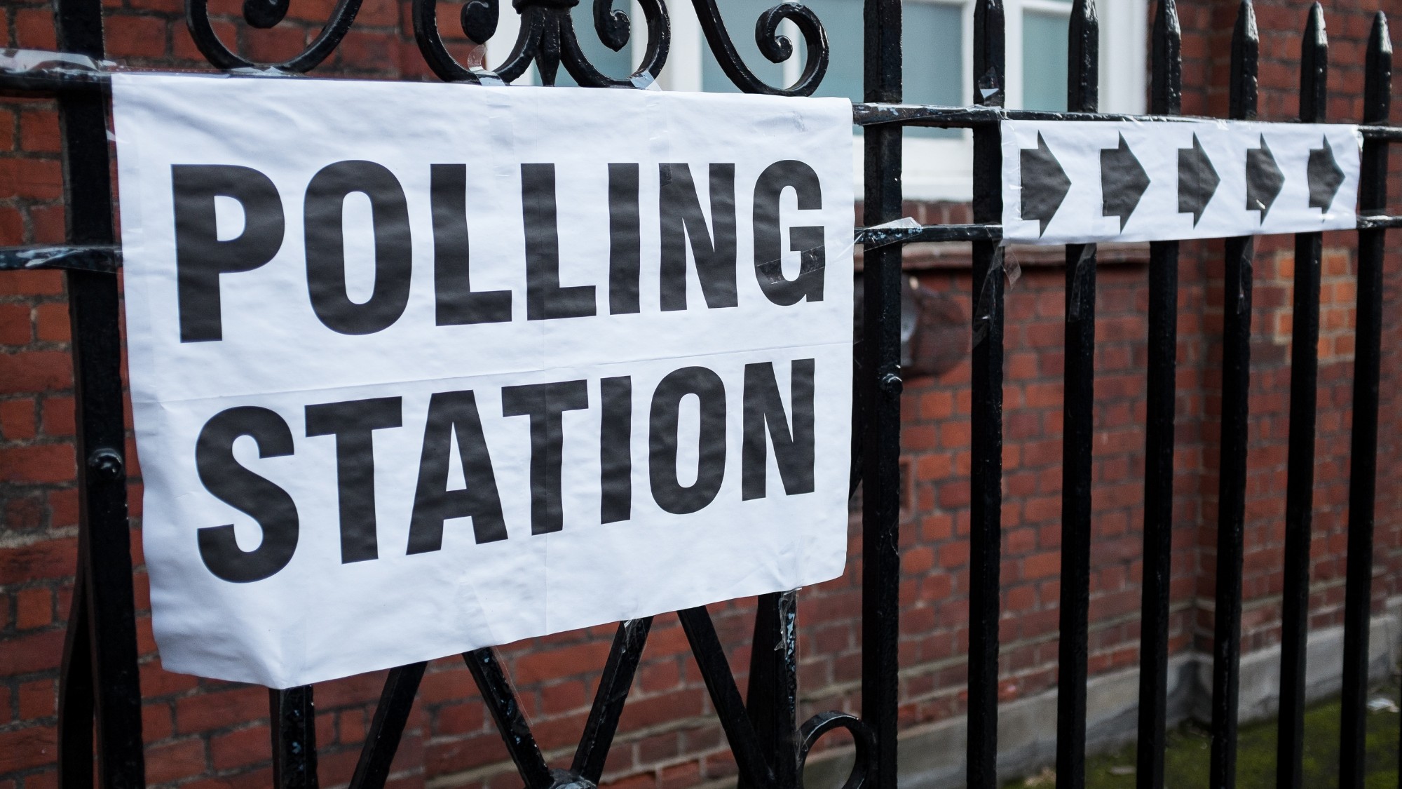 Democracy in the UK - polling station sign and arrows displayed on a metal fence
