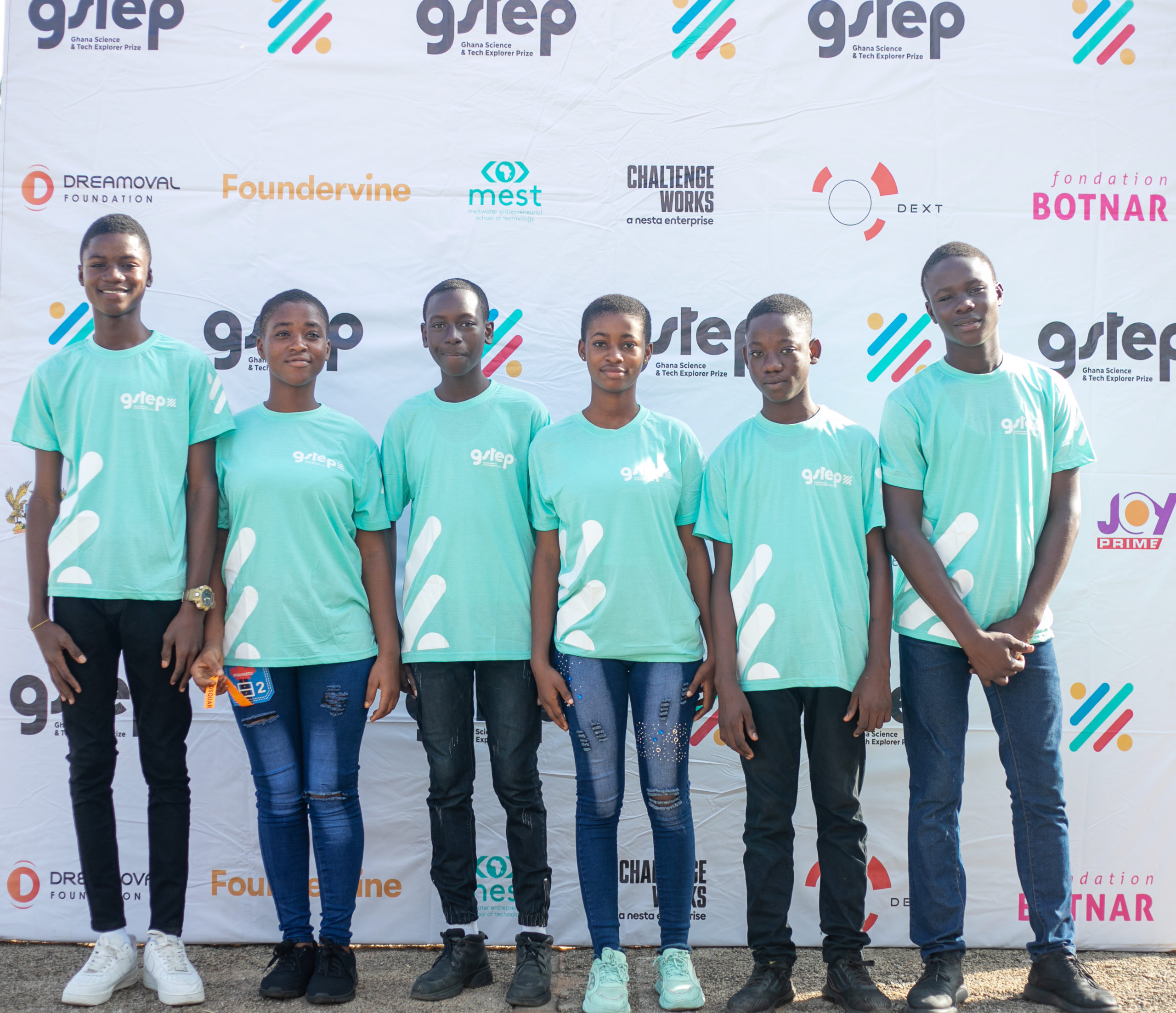 Group of young people in turquoise t-shirts standing in front of a printed banner