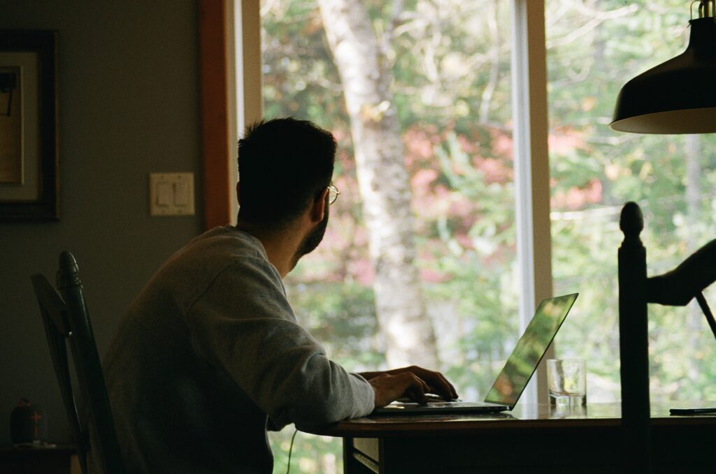 Man in grey T-shirt sat at a table with a laptop