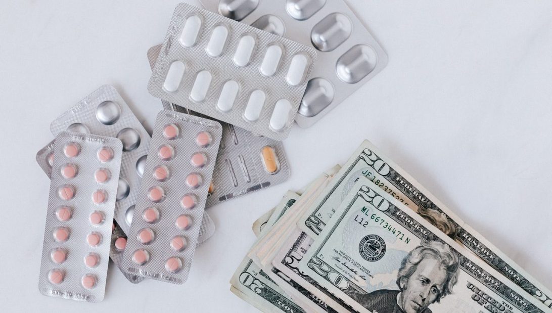 Silver blister packets of various pills next to a stack of American bank notes|Mary Millard